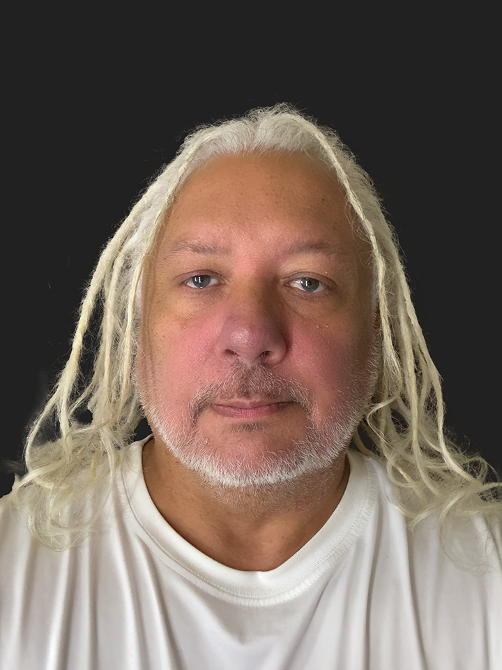 Elton. The Touring Eye. Creator of the Eyes Of Britain: Life Through 1,000 Eyes photography project. He is a Caucasian man with dreadlocks hanging down to his shoulders.